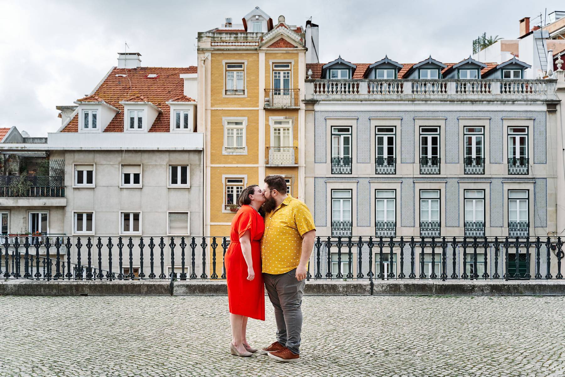 Michele &amp; Josh smooching in front of three buildings